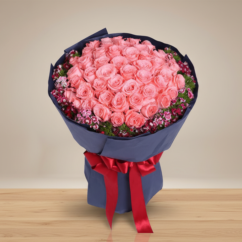 A bouquet of pink roses wrapped in navy paper with a red ribbon.
