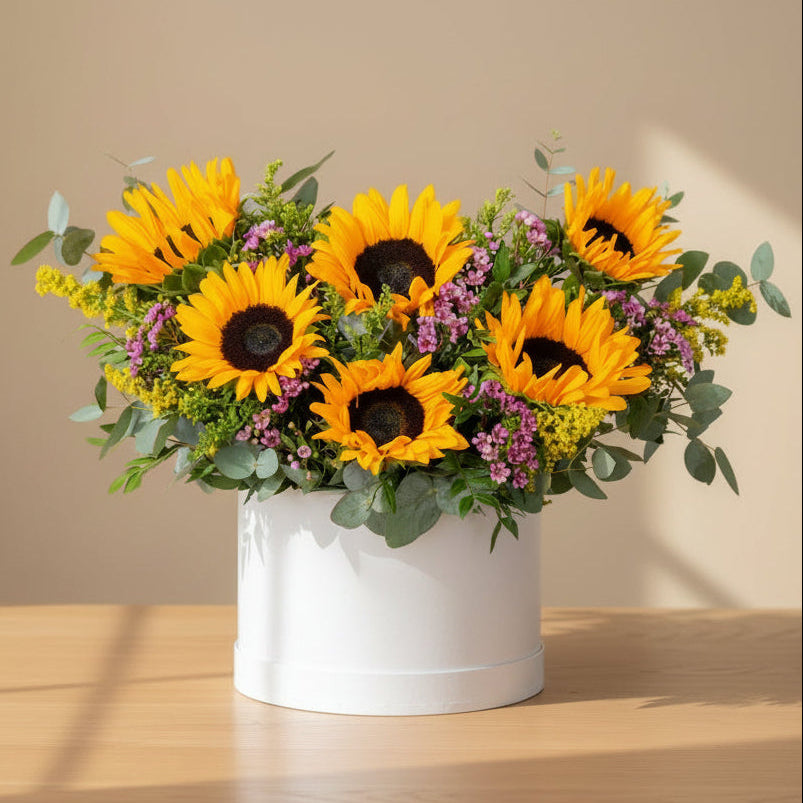 This arrangement is made of Sunflowers, eucalyptus, and pink wax flowers presented in our signature white flower box.