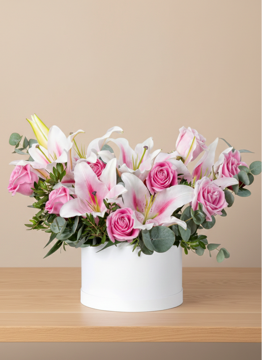 Floral arrangement with pink and white flowers in a white flower box on a wooden surface.