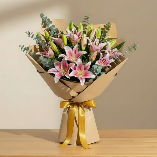 Bouquet of pink stargazer lilies wrapped in brown paper with a gold ribbon