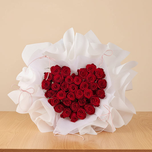 Heart-shaped bouquet of red roses wrapped in white paper