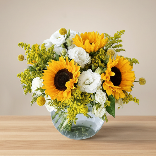 A vase arrangement of five sunflowers, white lisianthus and white spray roses, with greenery